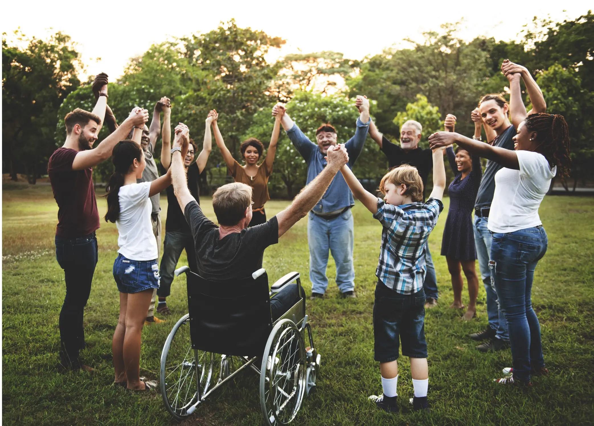 Inclusive community circle with wheelchair user raising hands together in a park